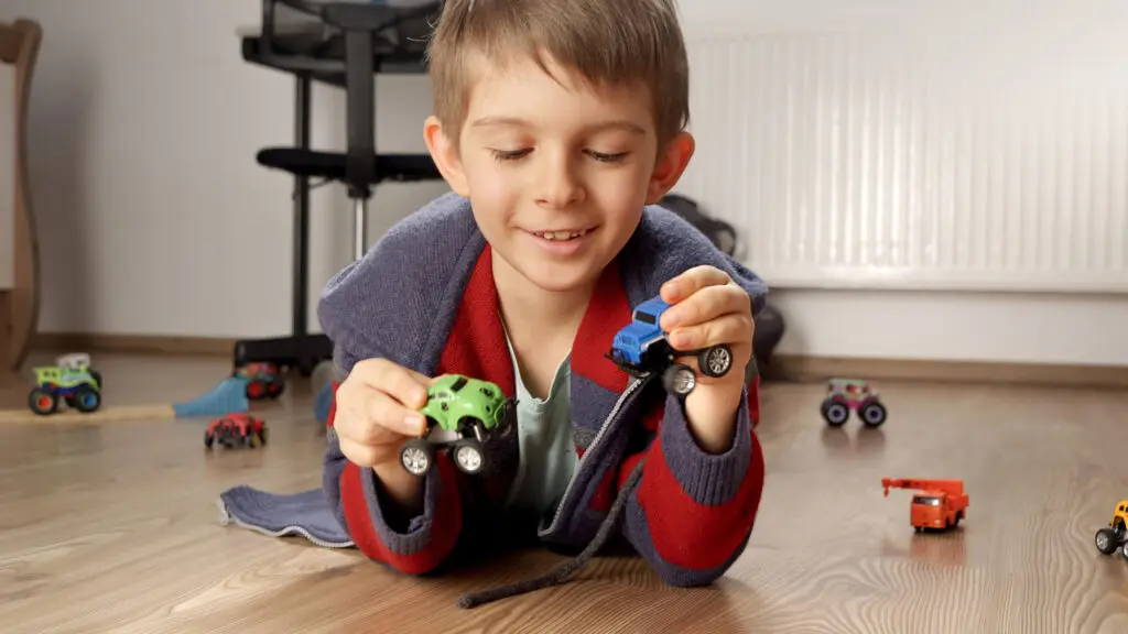 Happy smiling boy playing with his toys and cars while lying on floor in bedroom.