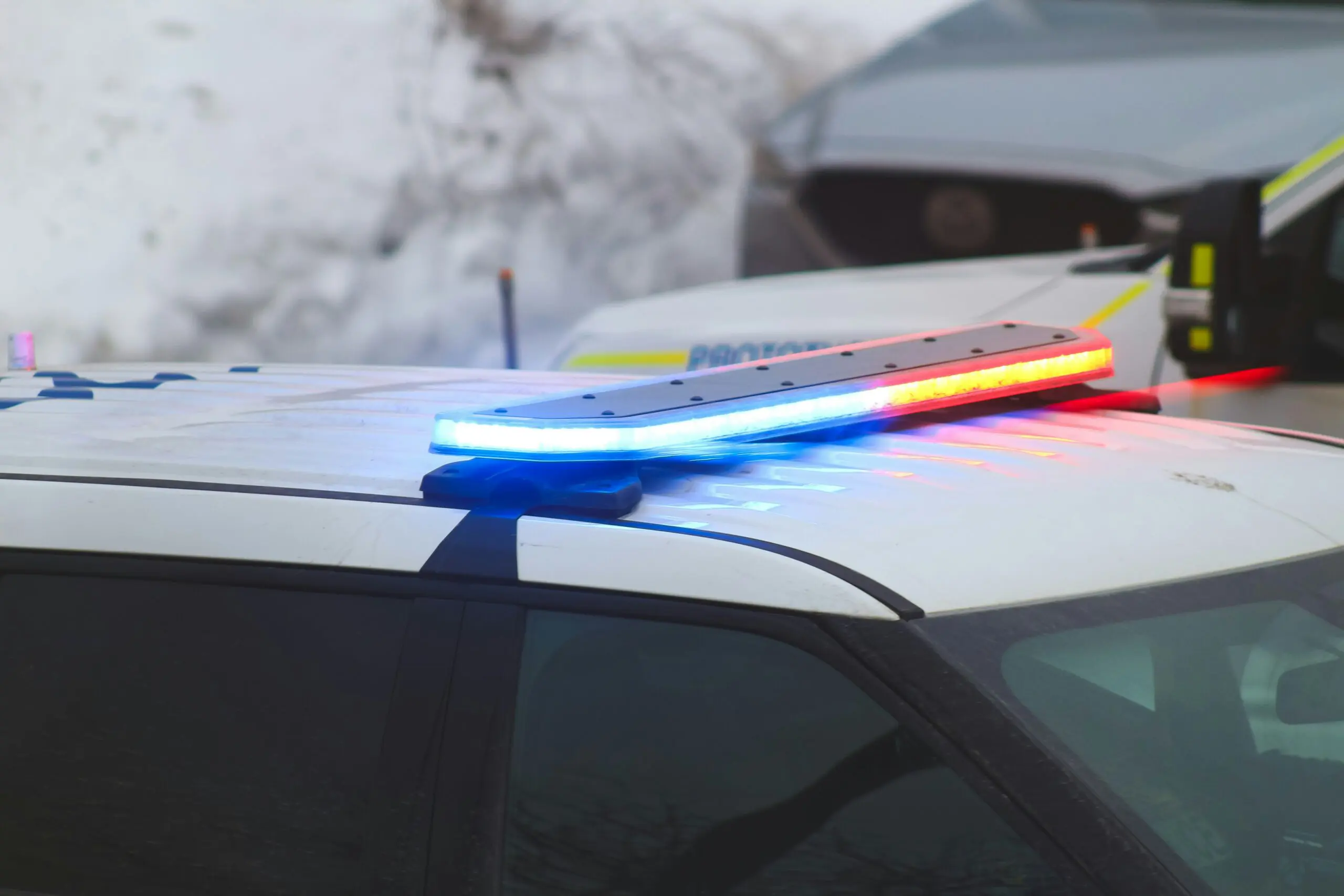 A police car with flashing lights on top, parked on the street, indicating an active response to an incident.