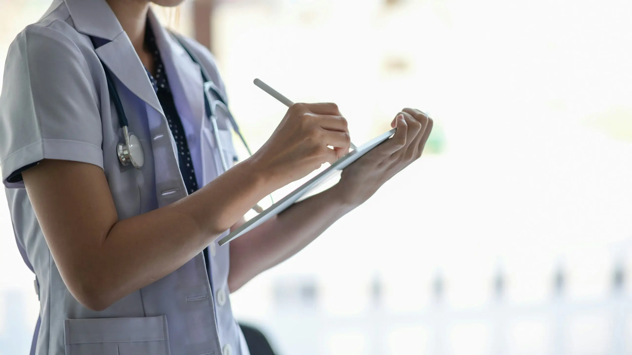 A female doctor writing notes on a clipboard in a clinical setting.