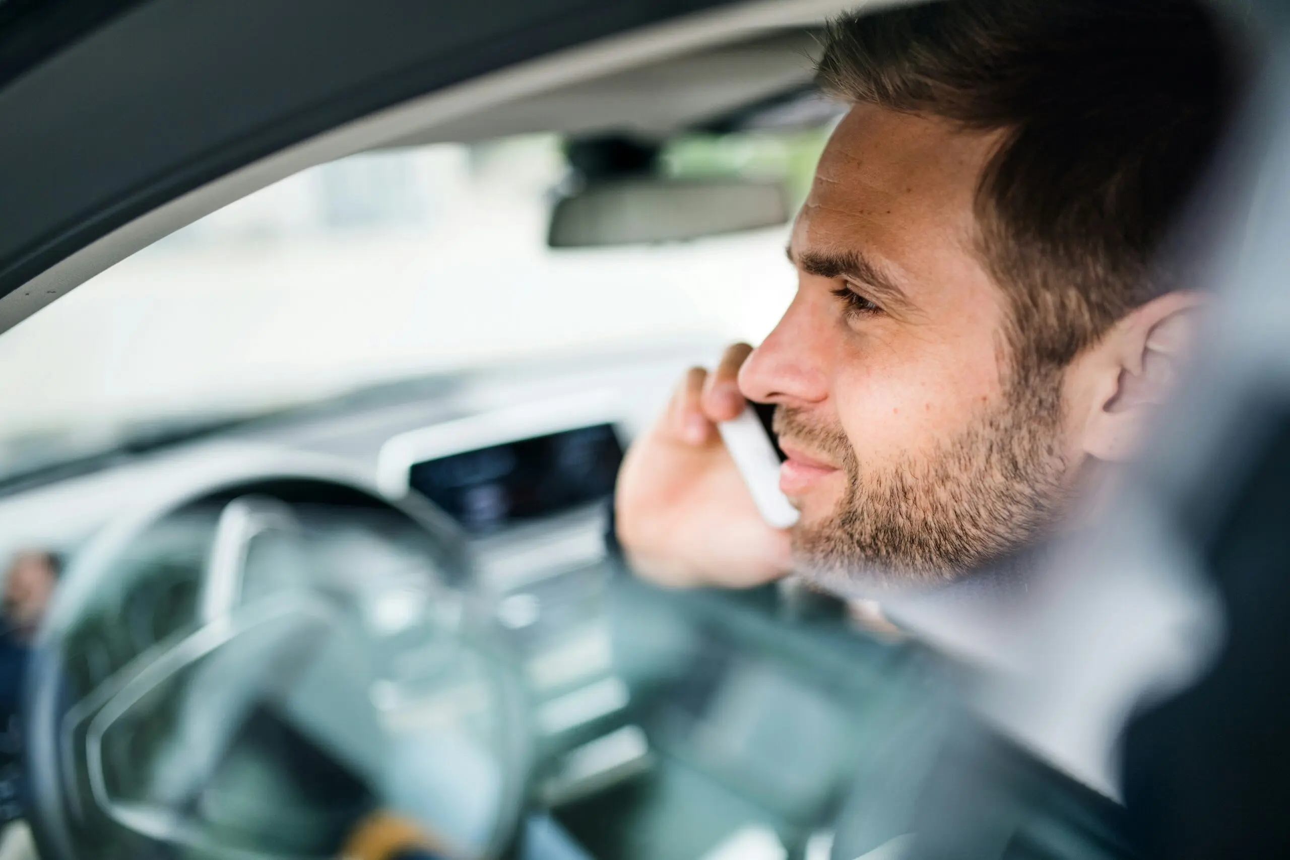 A man sitting in a car, engaged in a conversation on his cell phone.