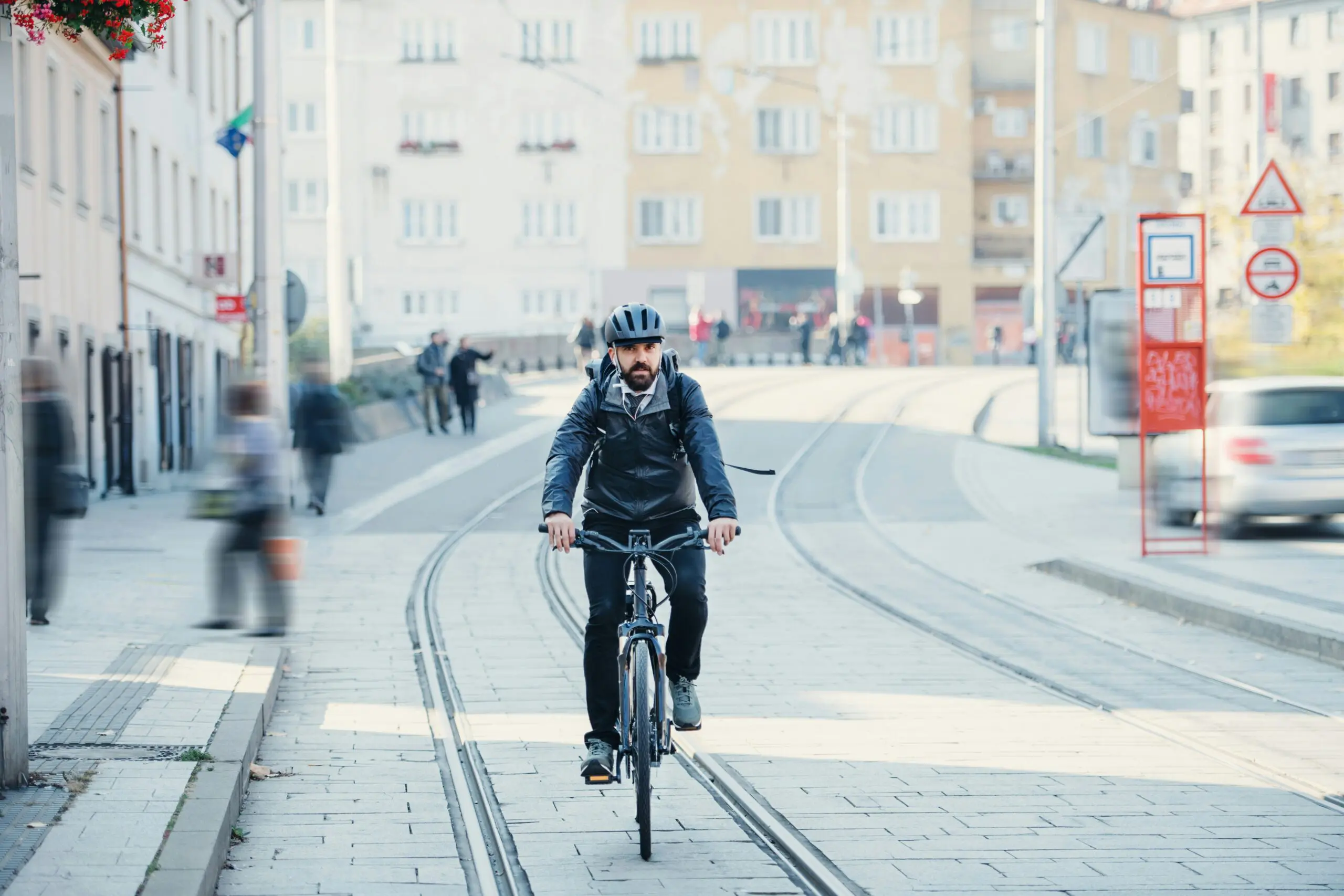 A man riding a bicycle along a busy city street, surrounded by buildings and pedestrians.