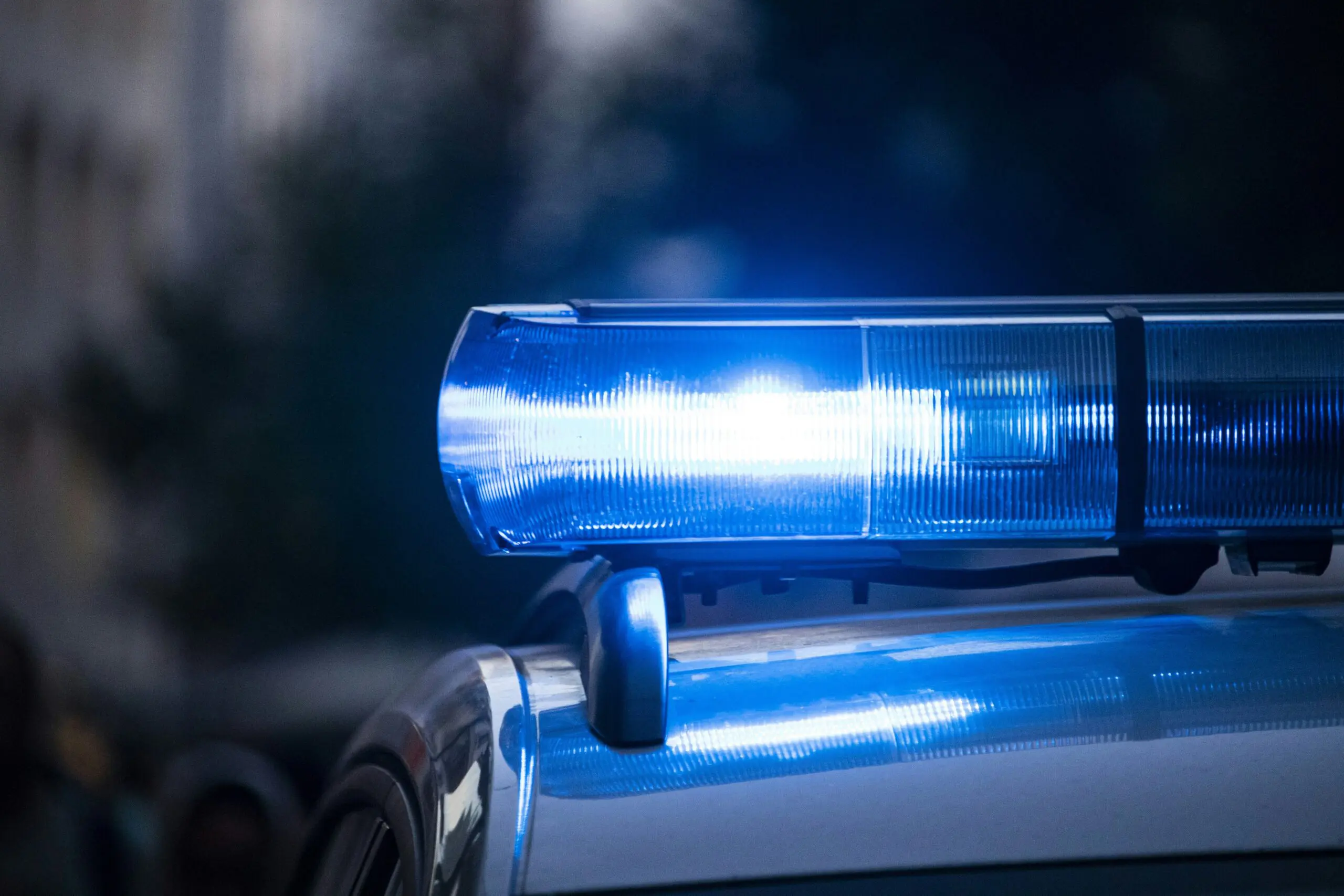 Close-up of a flashing blue police light mounted on top of a patrol car with a blurred background.