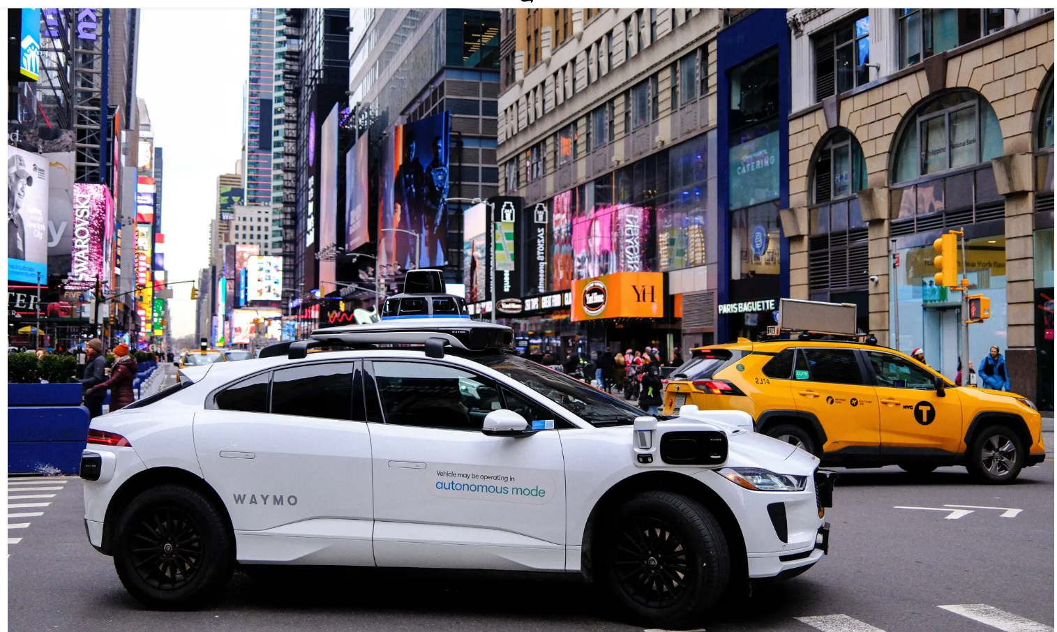 A self-driving car navigates a busy street filled with other vehicles and pedestrians.