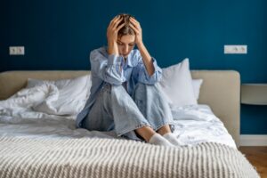 Woman sitting on a bed holding her head in distress