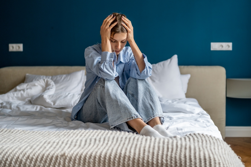 Woman sitting on a bed holding her head in distress