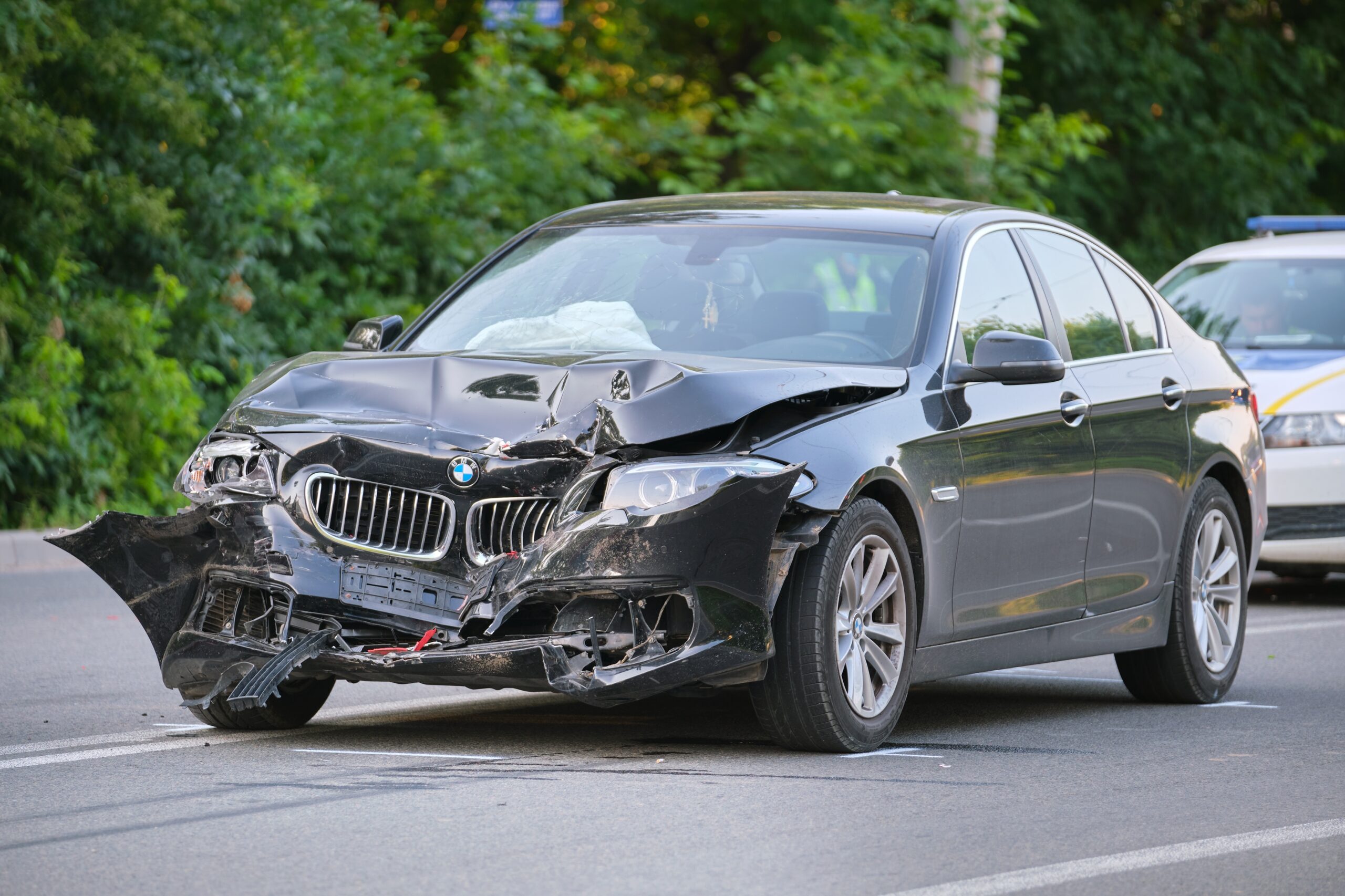 Black BMW sedan with severe front-end damage after a car accident, police vehicle in background